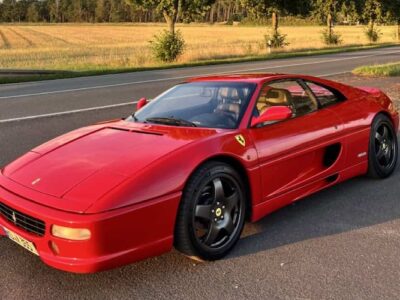 Red Ferrari F355 GTB parked in a scenic outdoor location, showcasing its sleek design and iconic shape.
